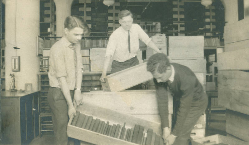 an image of a three staff members preparing for the Library's move to Superior Avenue, taken in around 1925. Three men carrying large bins of books