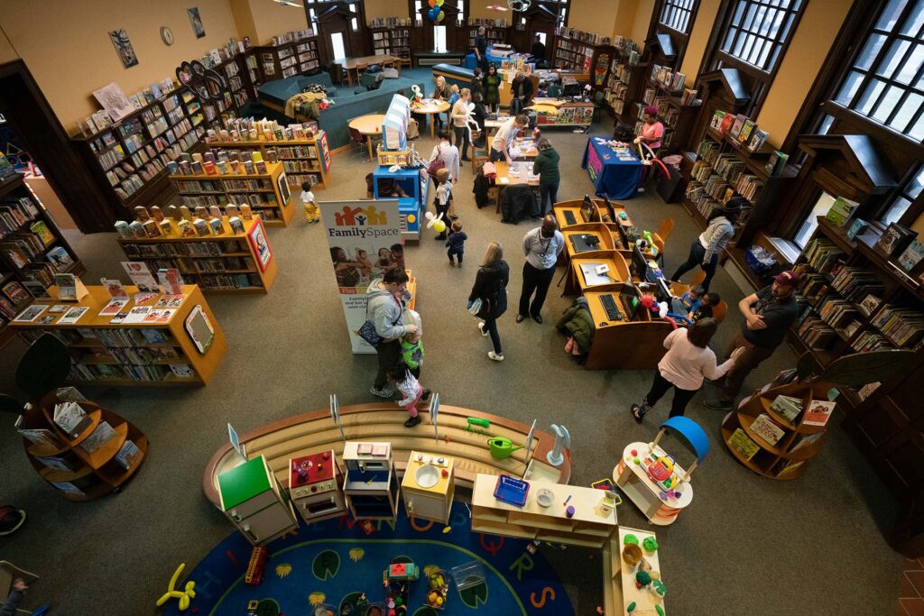 Aerial photo of children's room in carnegie west branch. Dozens of people walking around while children explore the books and toys