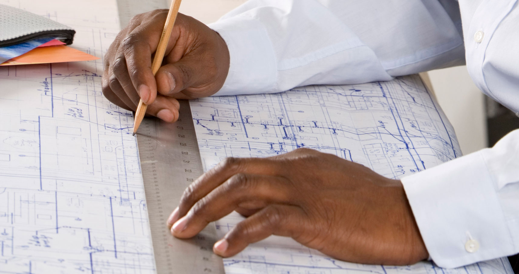 A man's hands drawing a blueprint on a drafting table.