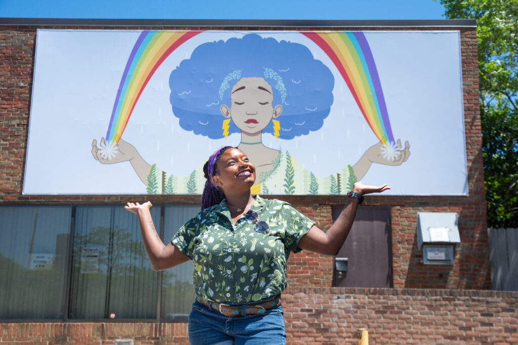 Artist Sequoia Bostick standing in front of her mural, imitating the mural.